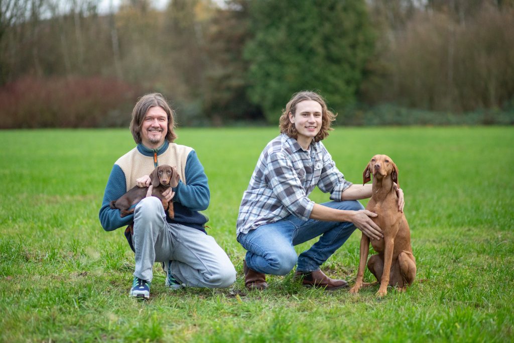 Zwei Personen mit ihren Hunden auf einer grünen Wiese im Freien