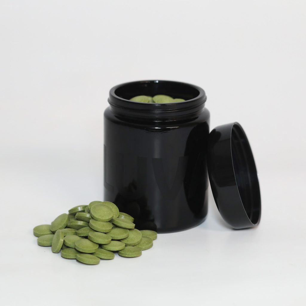 Luvano VAYNO Tabletten für Hunde in offenem schwarzen Violettglas mit grünen Presslingen