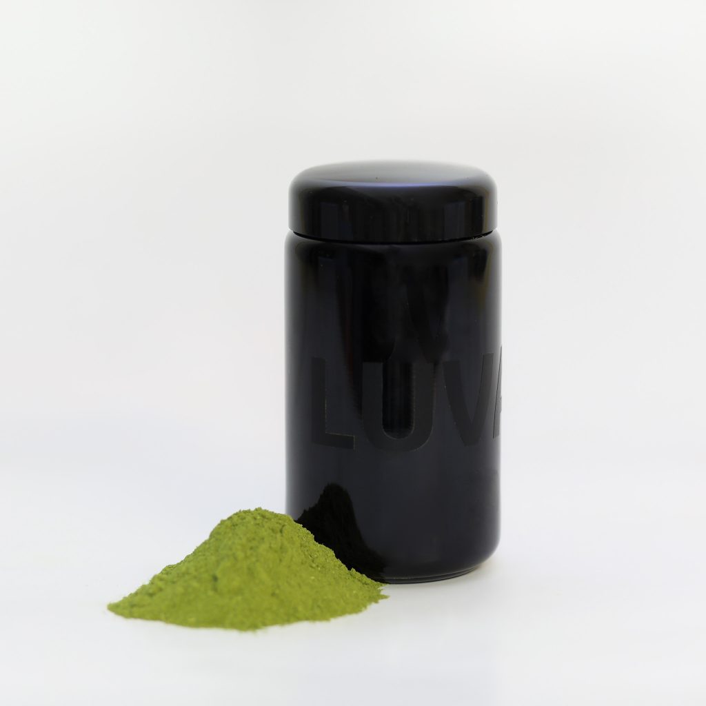 Geschlossenes Luvano Violettglas mit grünem Pulver, daneben aufgeschüttetes Ergänzungsfuttermittel für Hunde