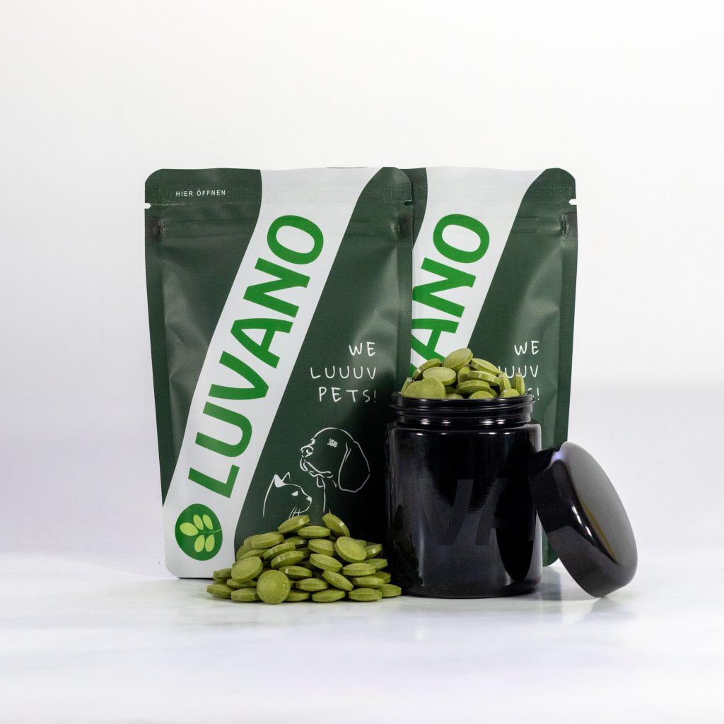 Luvano VAYNO Ergänzungsfuttermittel Tabletten für Hunde mit Standbeuteln und Tabletten im Glas vor hellem Hintergrund