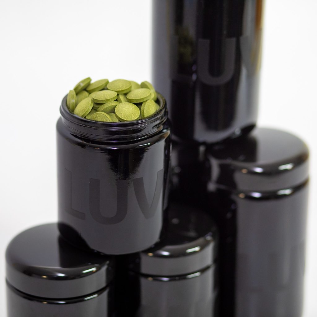 Geöffneter schwarzer Luvano Violettglasbehälter mit grünen Tabletten eines Ergänzungsfuttermittels für Hunde