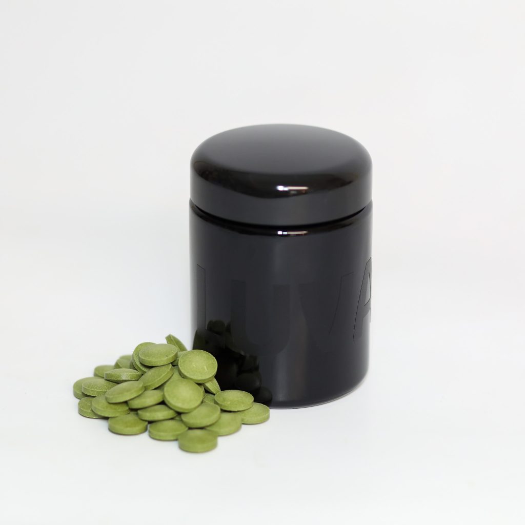 Schwarzer Luvano Violettglasbehälter mit grünen Tabletten eines Ergänzungsfuttermittels für Hunde