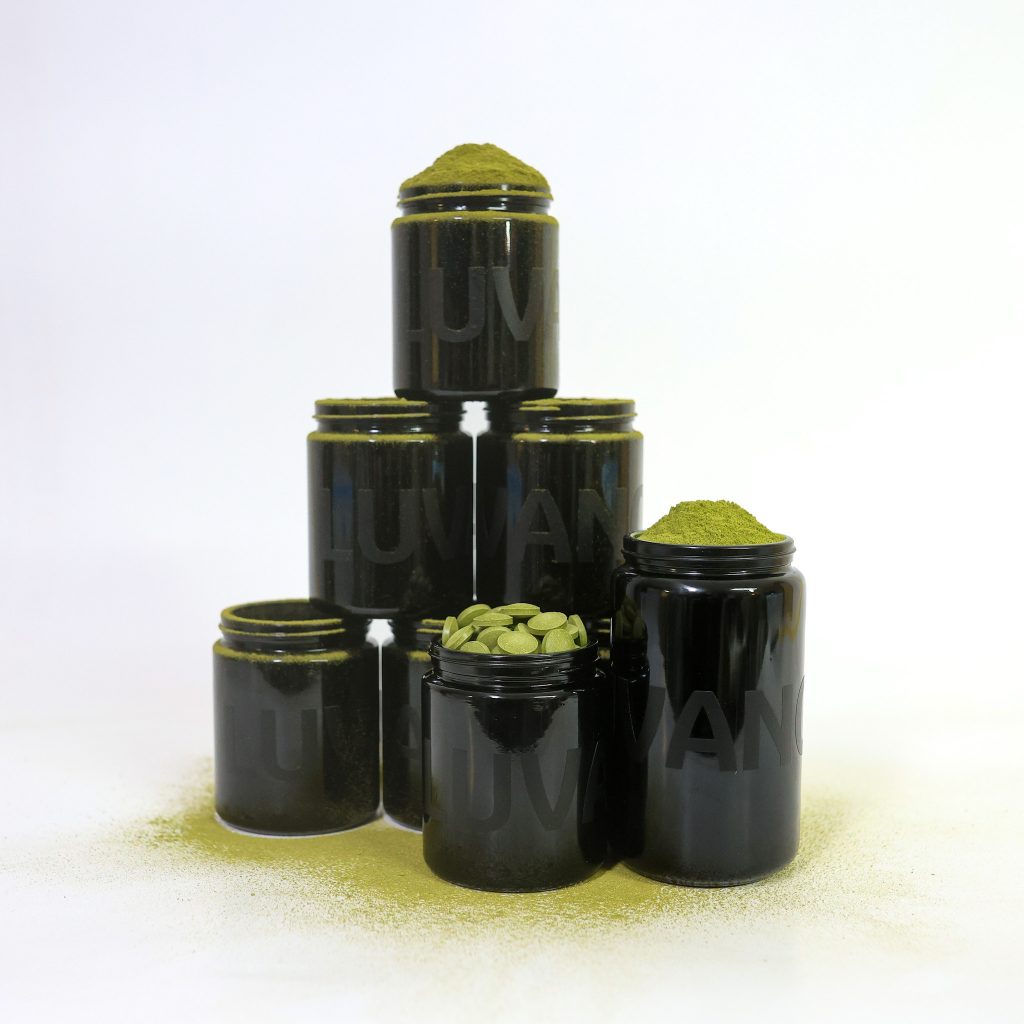 Mehrere schwarze Violettglasbehälter von Luvano, teilweise geöffnet und mit Pulver sowie Tabletten befüllt