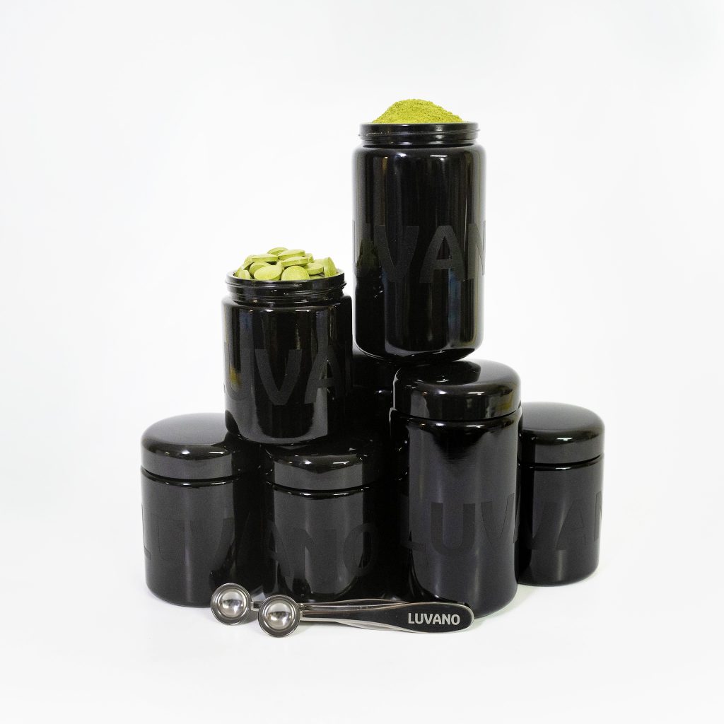 Mehrere schwarze Violettglasbehälter von Luvano mit Pulver, Tabletten und Dosierlöffel